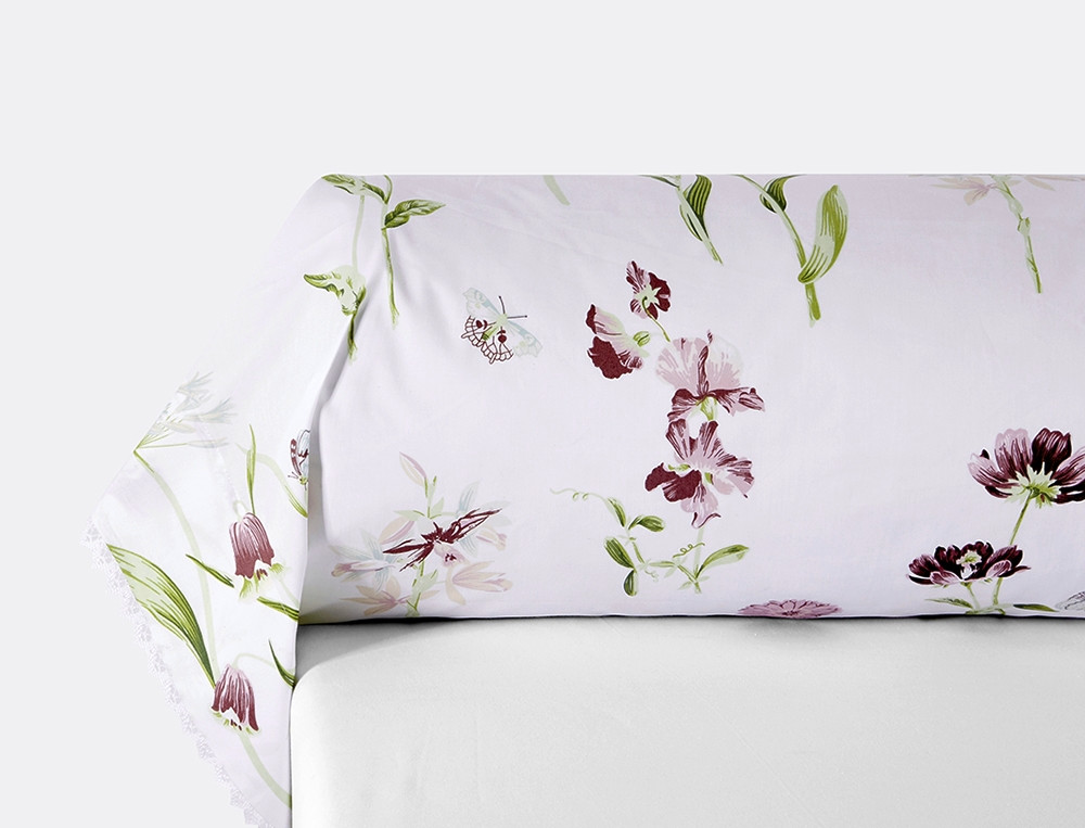 Une taie de traversin percale ornée de dentelle imprimée de fleurs et de papillons aux tons délicats sur fond blanc.